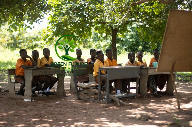 Pupils sitting at desks in the shade of a tree
