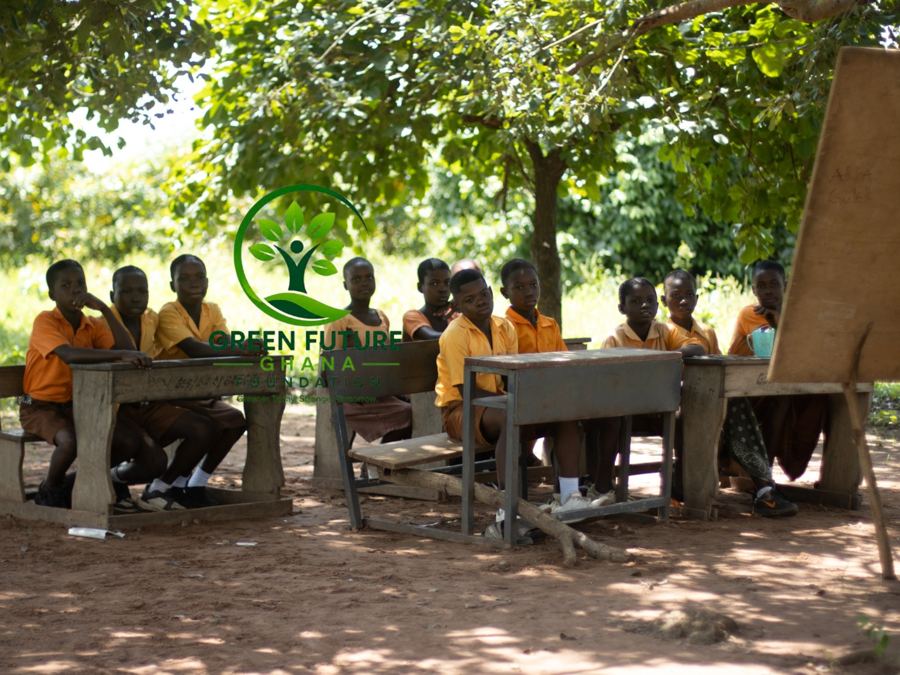 Pupils sitting at desks in the shade of a tree